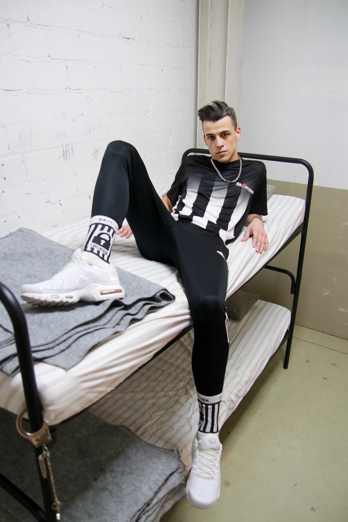 Urban look: model sits in a bunk bed in a prison cell wearing the Sk8erboy® Tikot and shiny track pants