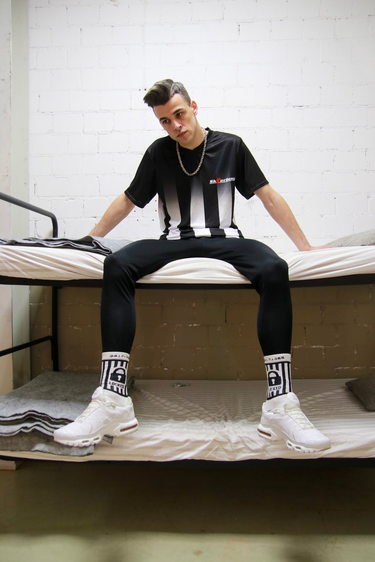 Urban look: model sitting in a bunk bed in a prison cell, wearing a Sk8erboy® T-shirt and shiny joggers