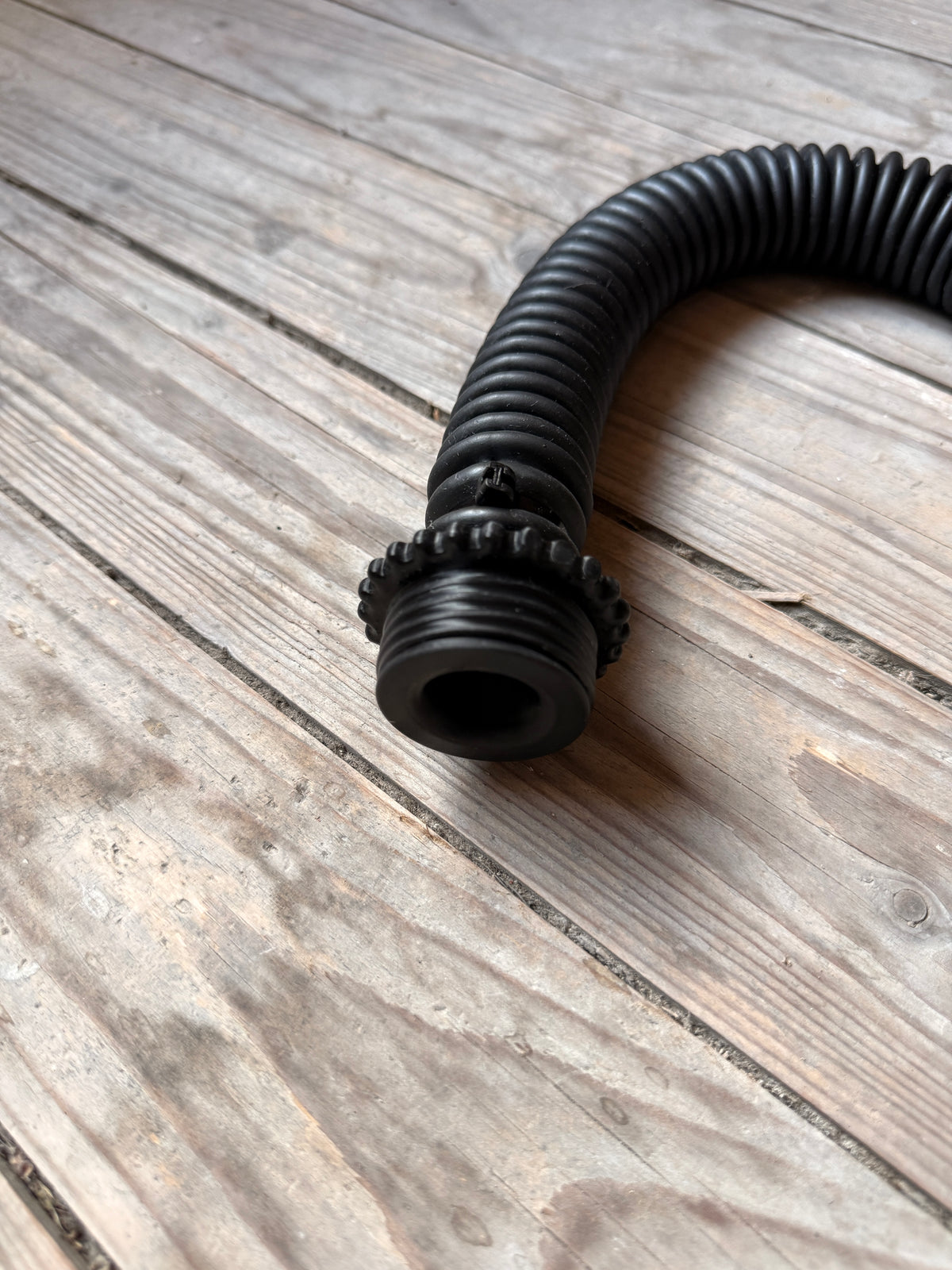 Gros plan du tuyau Vast Sniffer noir avec raccords vissés sur le parquet.