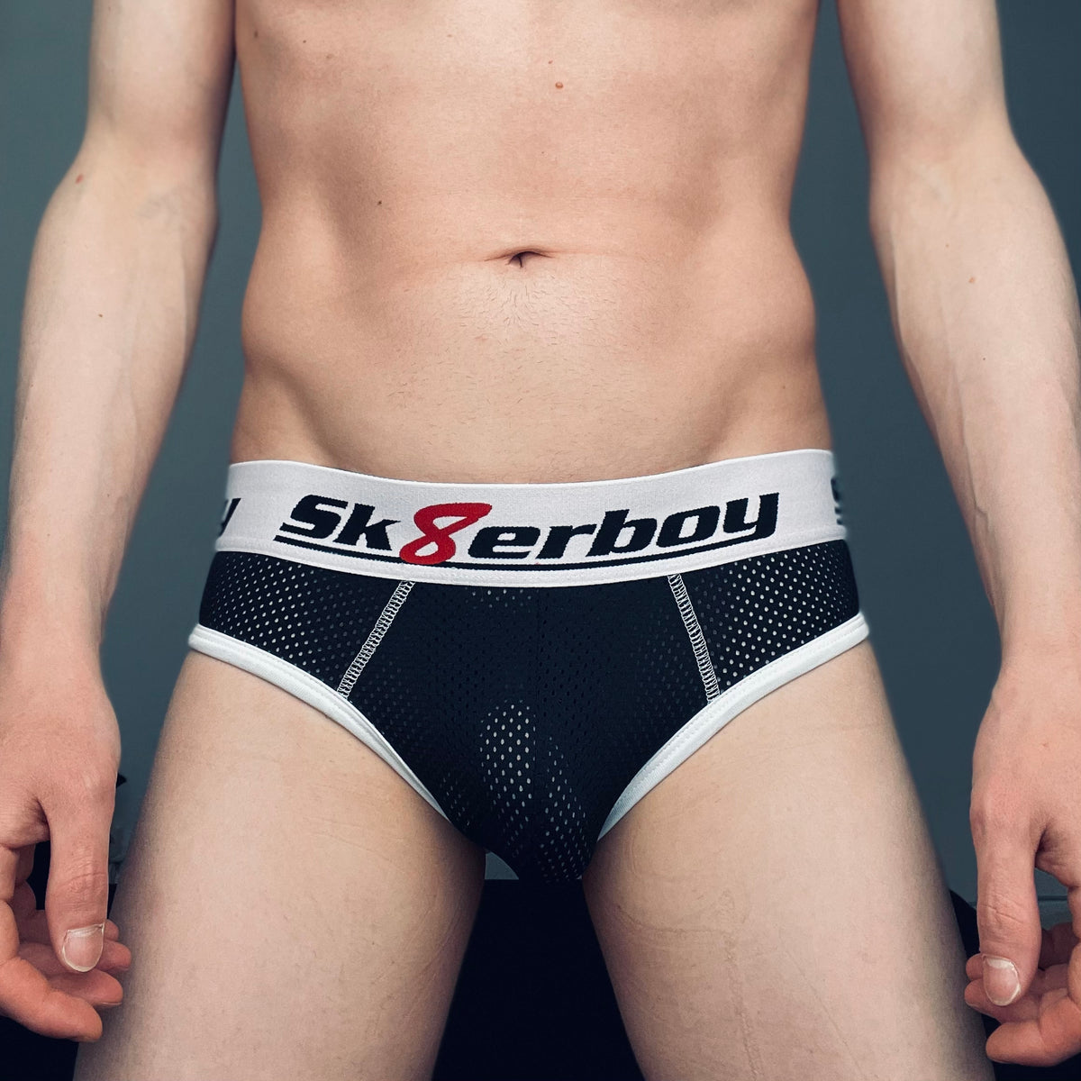 Jeune gay montrant son corps et portant un slip mesh noir à dos nu de sk8erboy avec grand logo sur la large ceinture