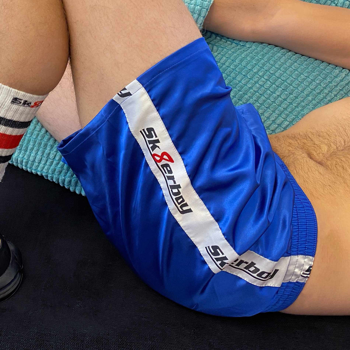 Jeune homme allongé sur le canapé, se tortillant et frottant ses chaussettes tube Sk8erboy smelly sexy sur son boxer bleu royal brillant à large bande satinée.