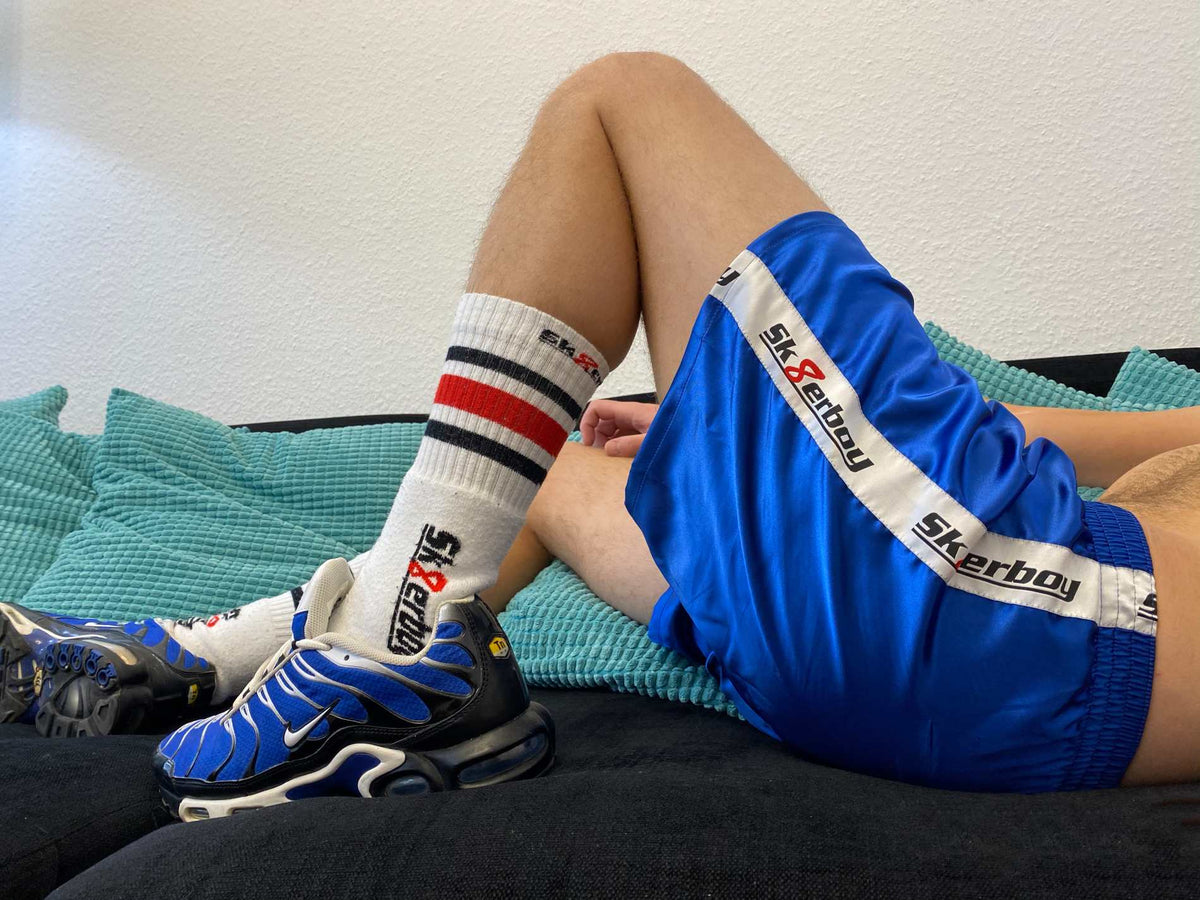 garçon allongé sur le canapé qui se tortille et frotte ses chaussettes tube Sk8erboy puantes et sexy contre son boxer bleu roi brillant, avec une large bande satinée