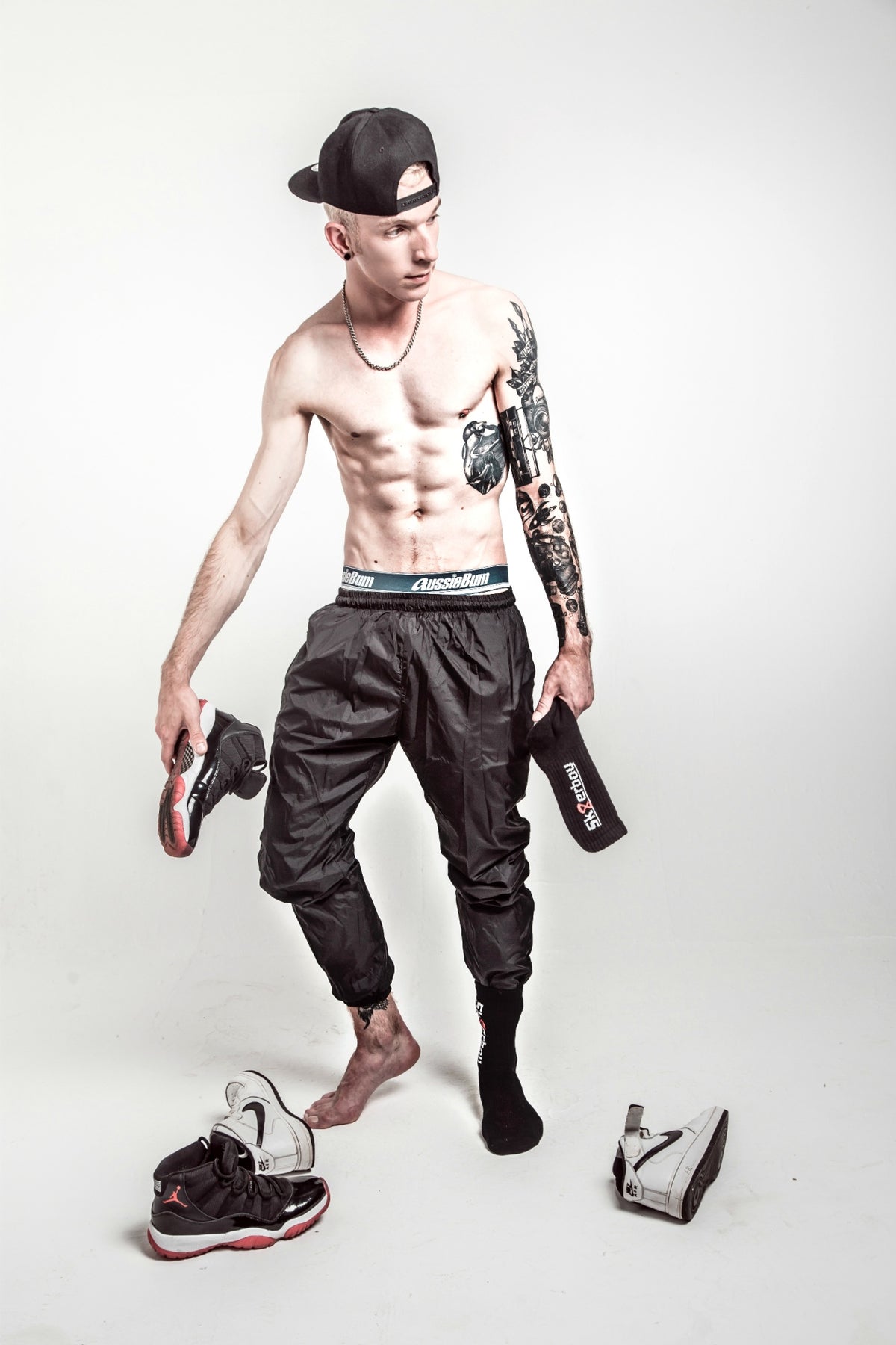 sporty young man with bare chest wears black track pants and aussiebom shorts with black crew socks from sk8erboy in his Jordan sneakers