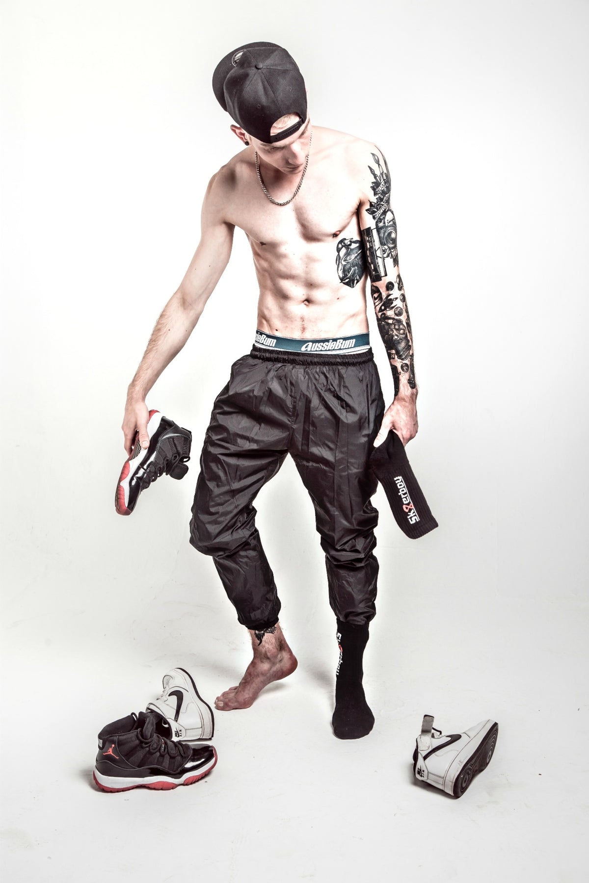 athletic young man with a tattoo on his arm wearing black sports shorts and matching black crew socks from sk8erboy with his Nike Jordan sneakers