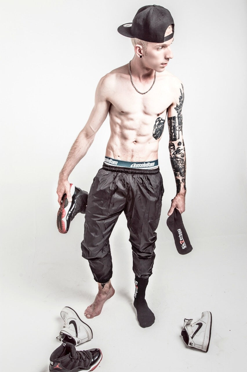 bare-chested sporty young man wearing a black cap and sportswear, holding black crew socks by sk8erboy in his hand and wearing his Nike sneakers on his feet