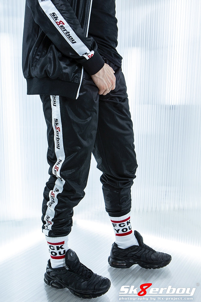 jeune homme avec pantalon noir brillant de sk8erboy, veste assortie, chaussettes fck you de sk8erboy et sneakers Nike-TN