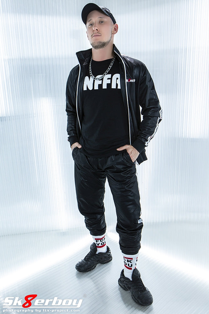 jeune homme gay montrant son survêtement brillant ouvert tracksuits de sk8erboy avec t-shirt snffr noir et chaussettes fck you dans des Nike TN avec casquette