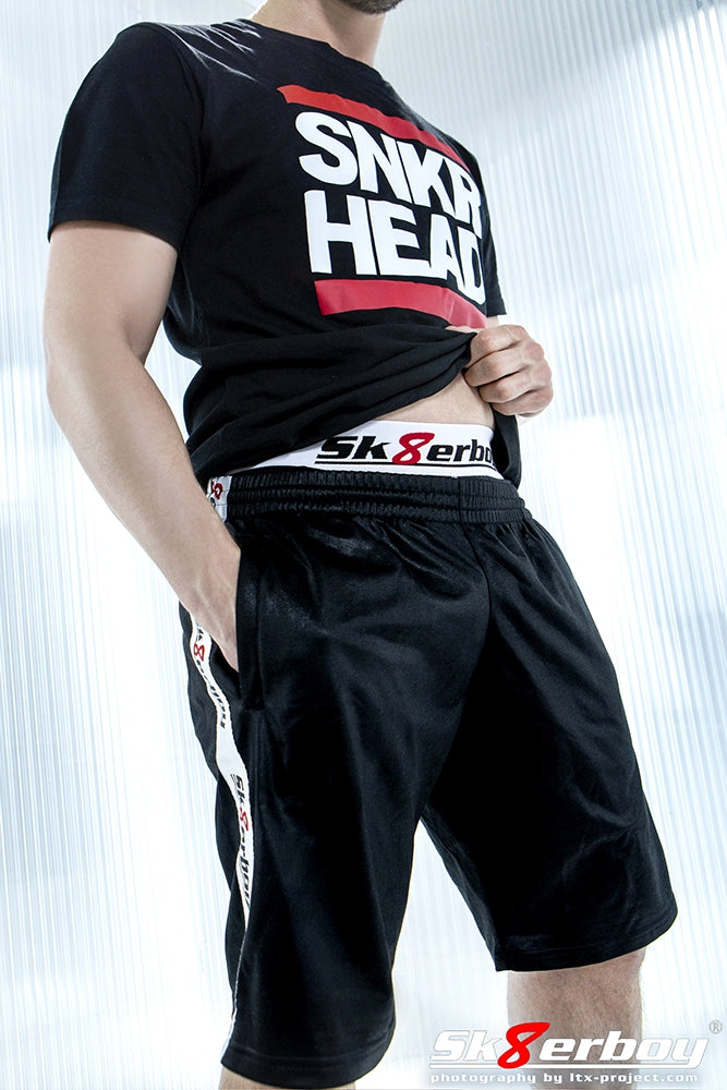 Jeune homme portant un short brillant Sk8erboy et un boxer assorti, avec un T-shirt noir Snekr Sneaker Head à imprimé blanc et bandes rouges