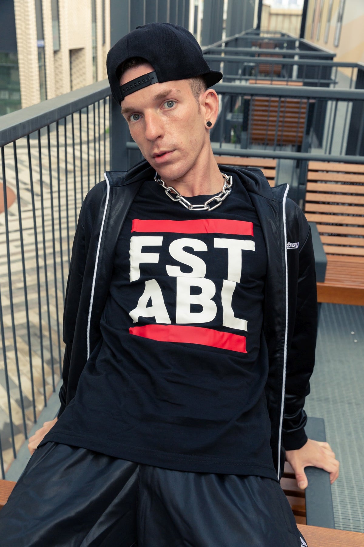 young boy on a terrace wearing a shiny Sk8erboy tracksuit with a black T-shirt featuring a large FST ABL print