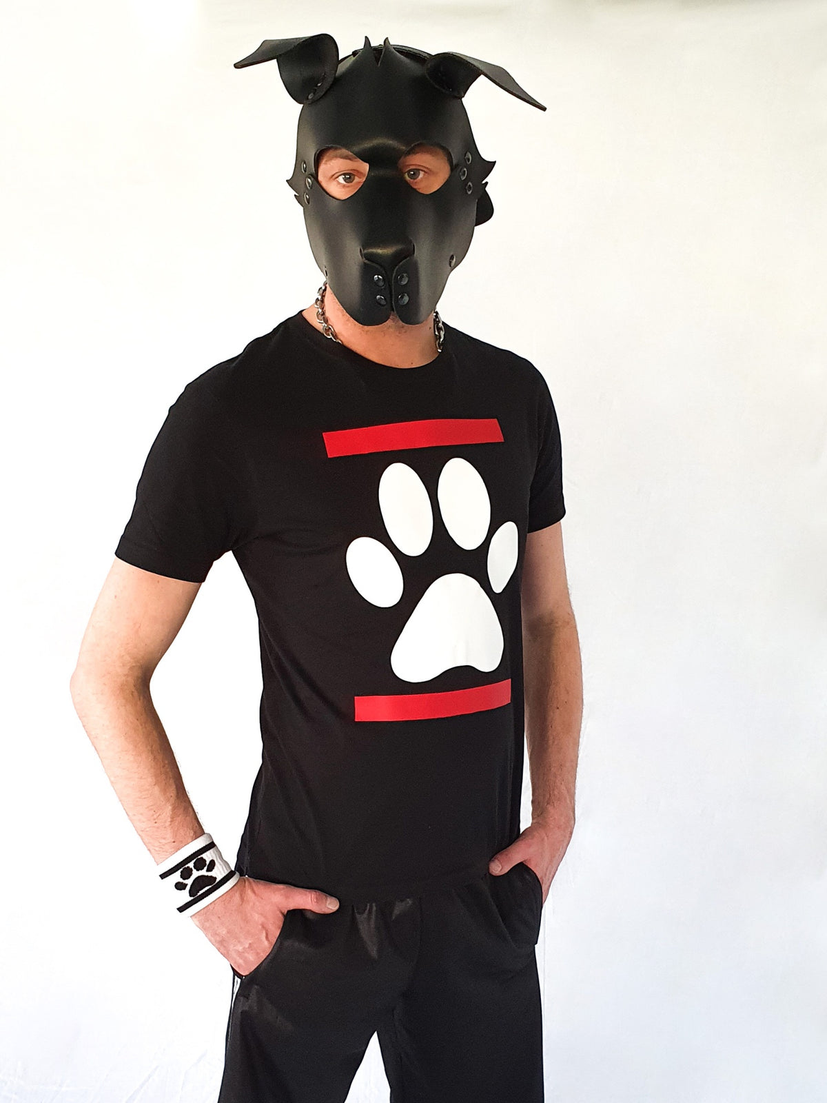 Un jeune homme portant un grand collier porte un masque de chien Mister B en cuir, un t-shirt Sk8erboy Dog Paw Puppy avec une photo de chien blanche entre deux bandes rouges et un pantalon de survêtement Sk8erboy Shiny confortable.