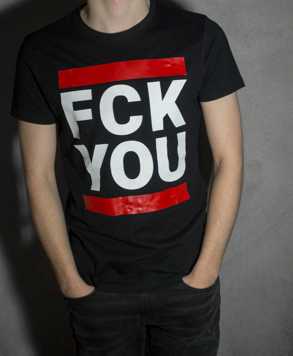 Jeune homme devant un mur, portant un T-shirt noir Sk8erboy avec l’inscription « fck you » en grandes lettres blanches barrées de rouge