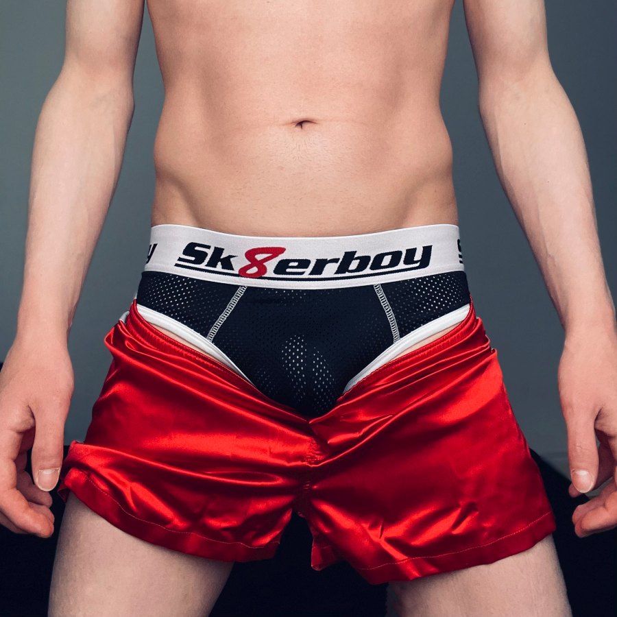 Jeune homme gay montrant son corps et portant un sous-vêtement noir en mesh à l’arrière ouvert, de sk8erboy, avec grand logo sur la large ceinture