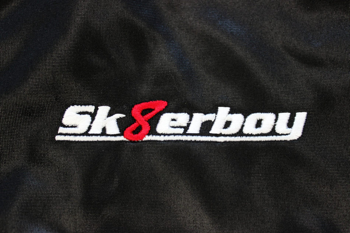 Gros plan du logo sk8erboy brodé sur la veste brillante noire, avec écriture blanche et huit rouge.