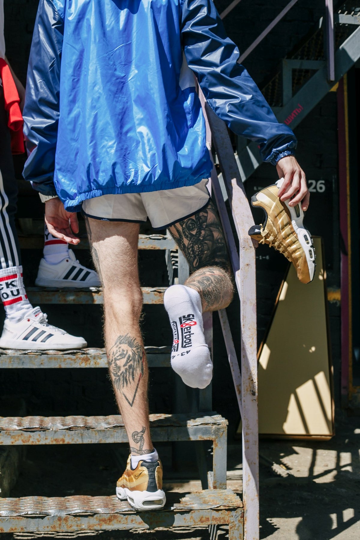gay man with tattoo from behind on a staircase wearing white sneaker socks by sk8erboy and FCK YOU socks in Nike and Adidas sneakers