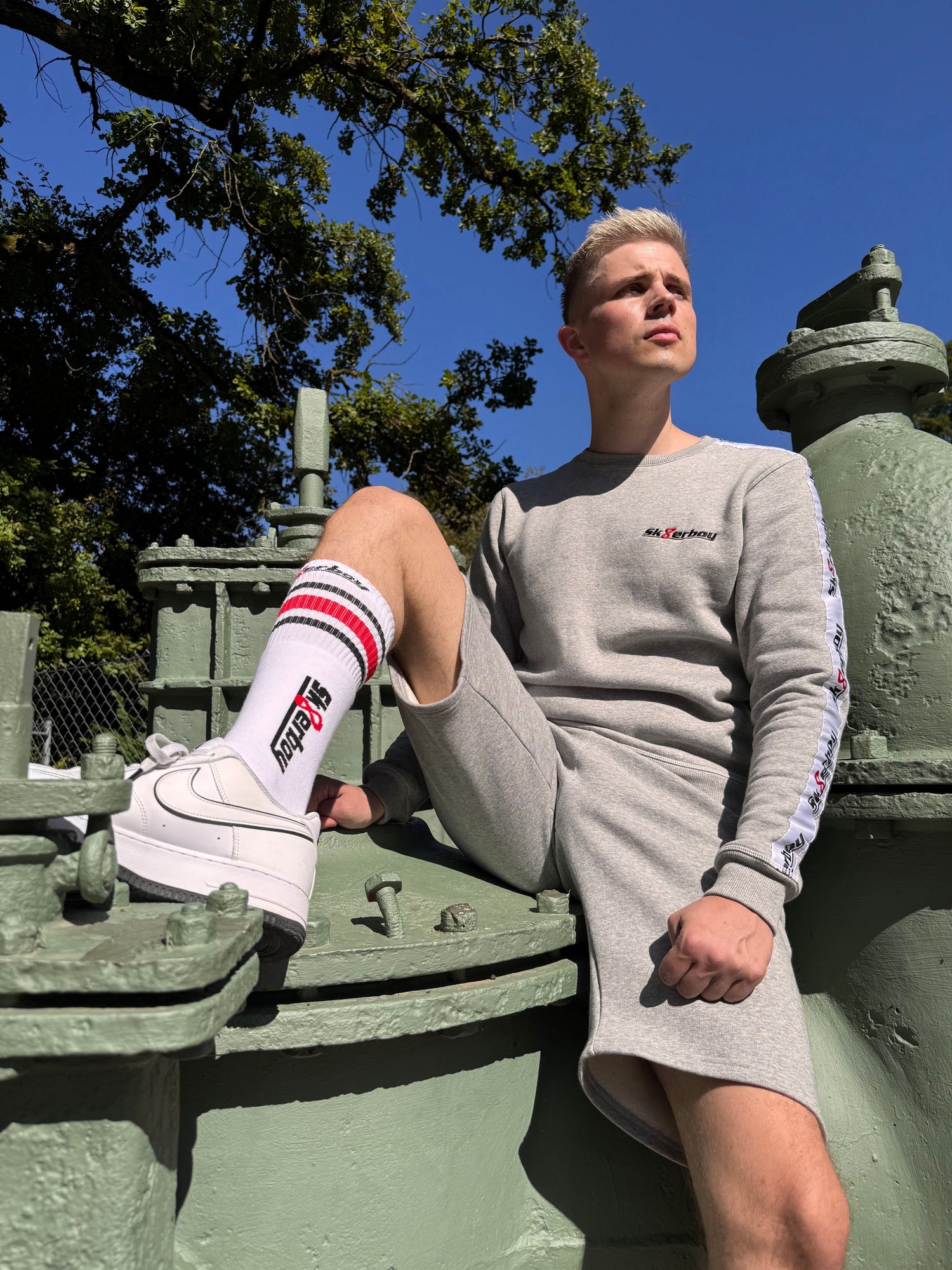 Junger Typ in einem Loft trägt einen Shiny Jogginganzug von Sk8erboy mit Basecap und nike sneaker sehr lässig