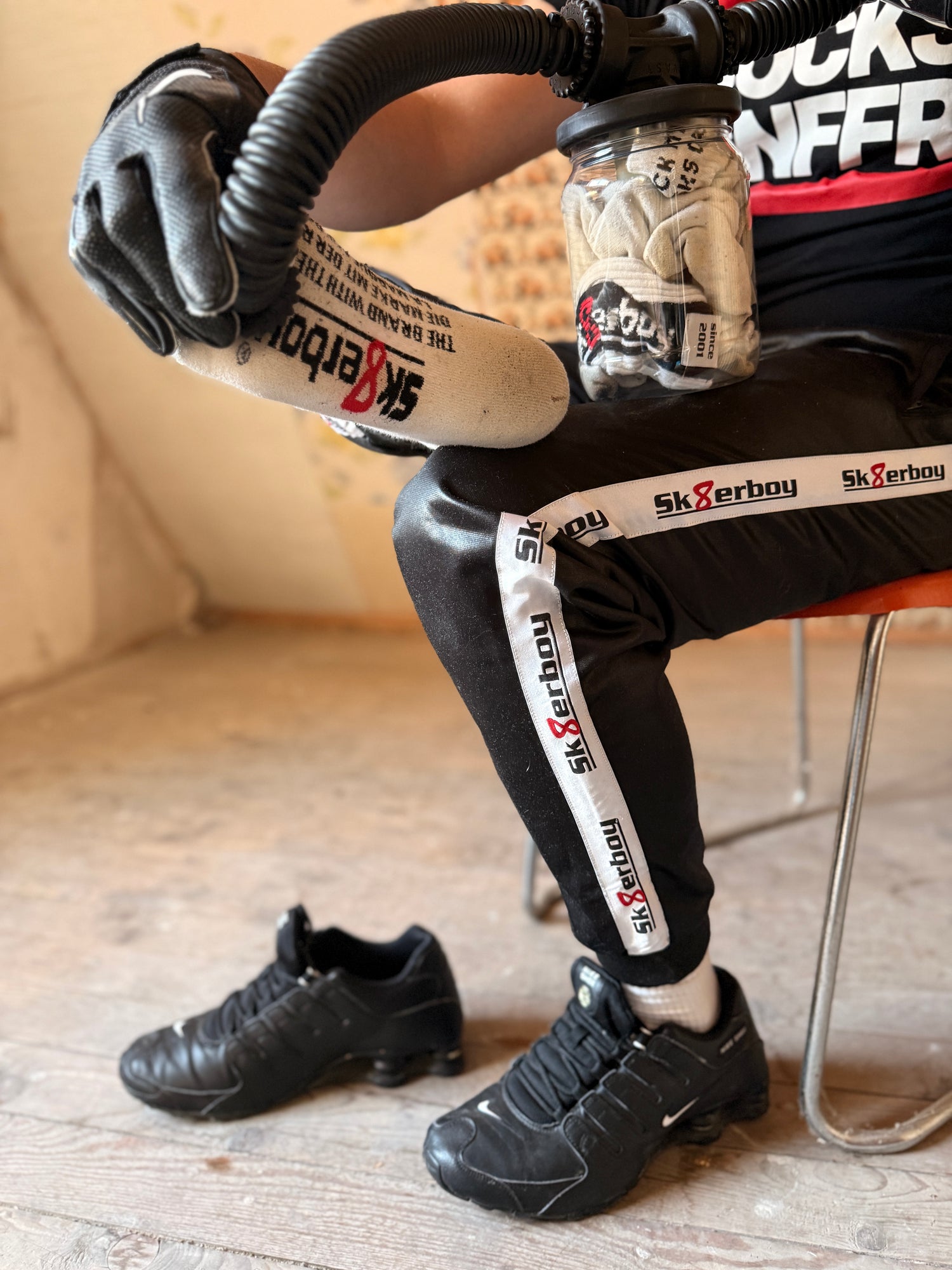 Person mit Sk8erboy Trainingshose und Vast Sniffer Glas, in der Hand ein weißer Sk8erboy Socken über den Schlauch gestülpt zum sniffen.