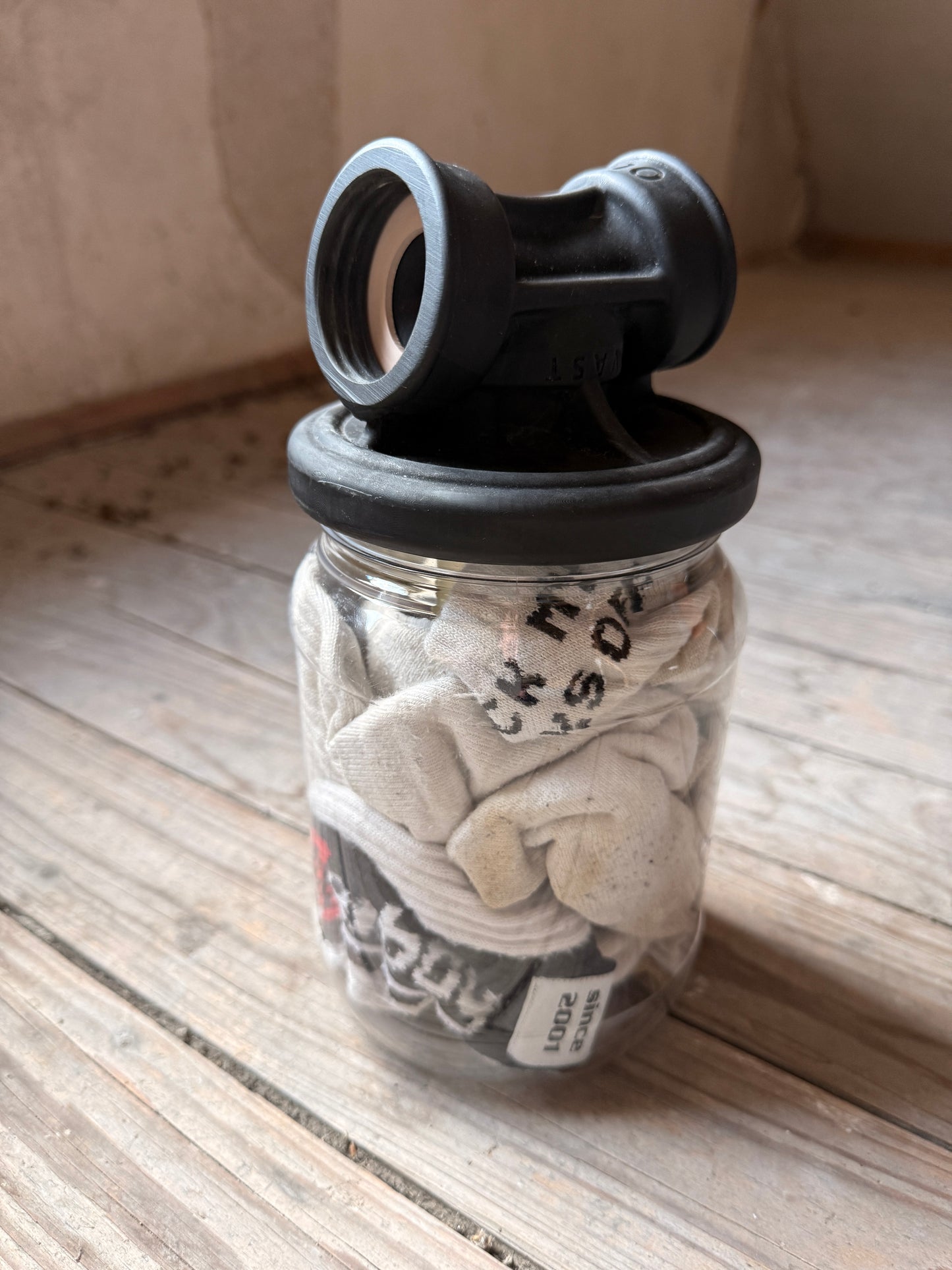 Sk8erboy Vast Sniffer Glas gefüllt mit weißen, getragenen Socken auf einem Holzboden.