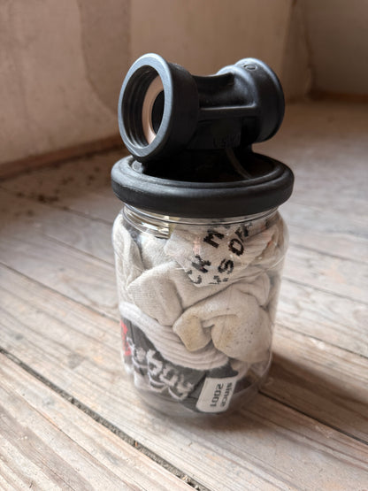 Sk8erboy Vast Sniffer Glas gefüllt mit weißen, getragenen Socken auf einem Holzboden.