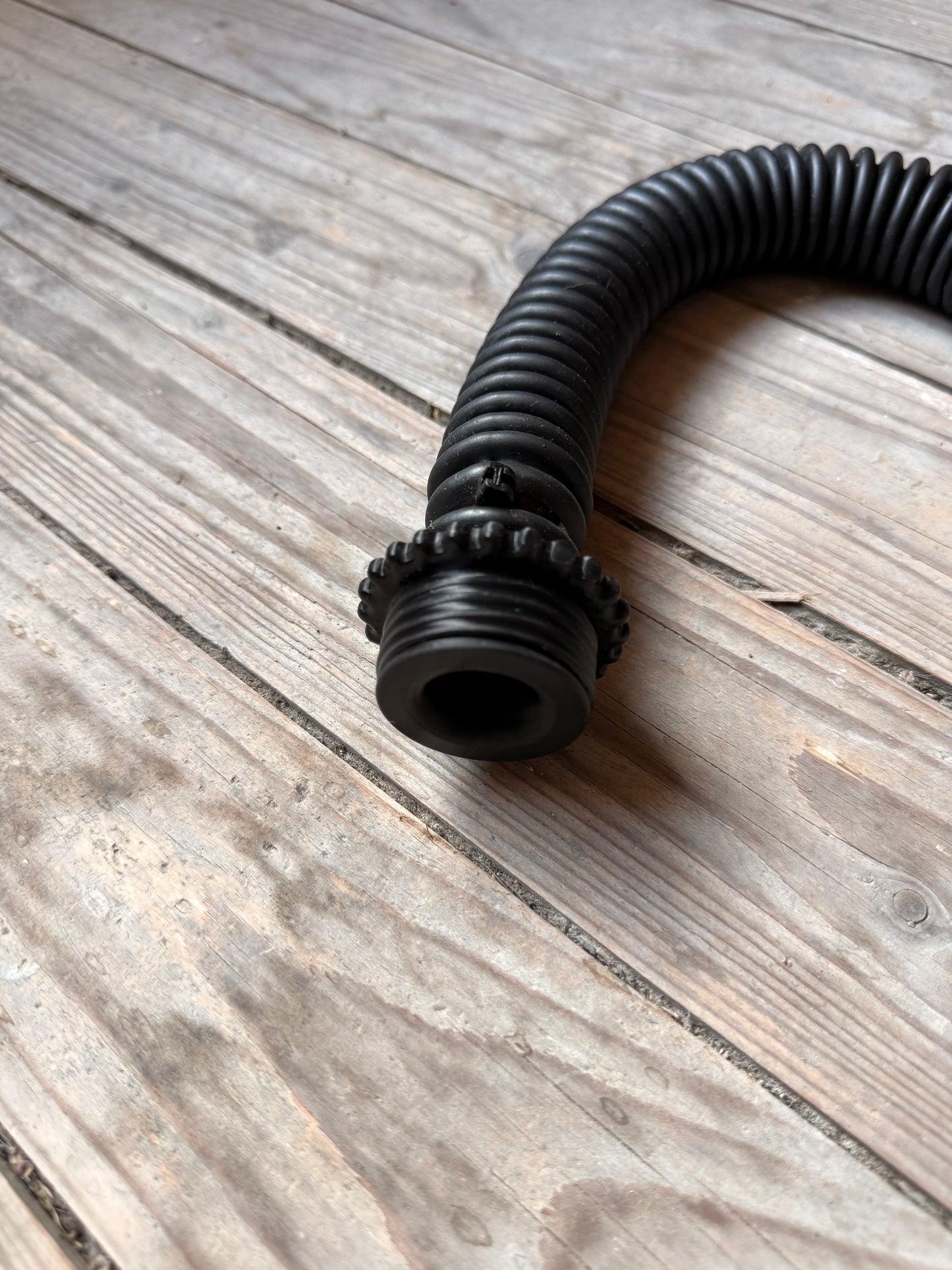 Detailaufnahme des schwarzen Vast Sniffer Schlauchs mit Schraubanschlüssen auf dem Holzboden.