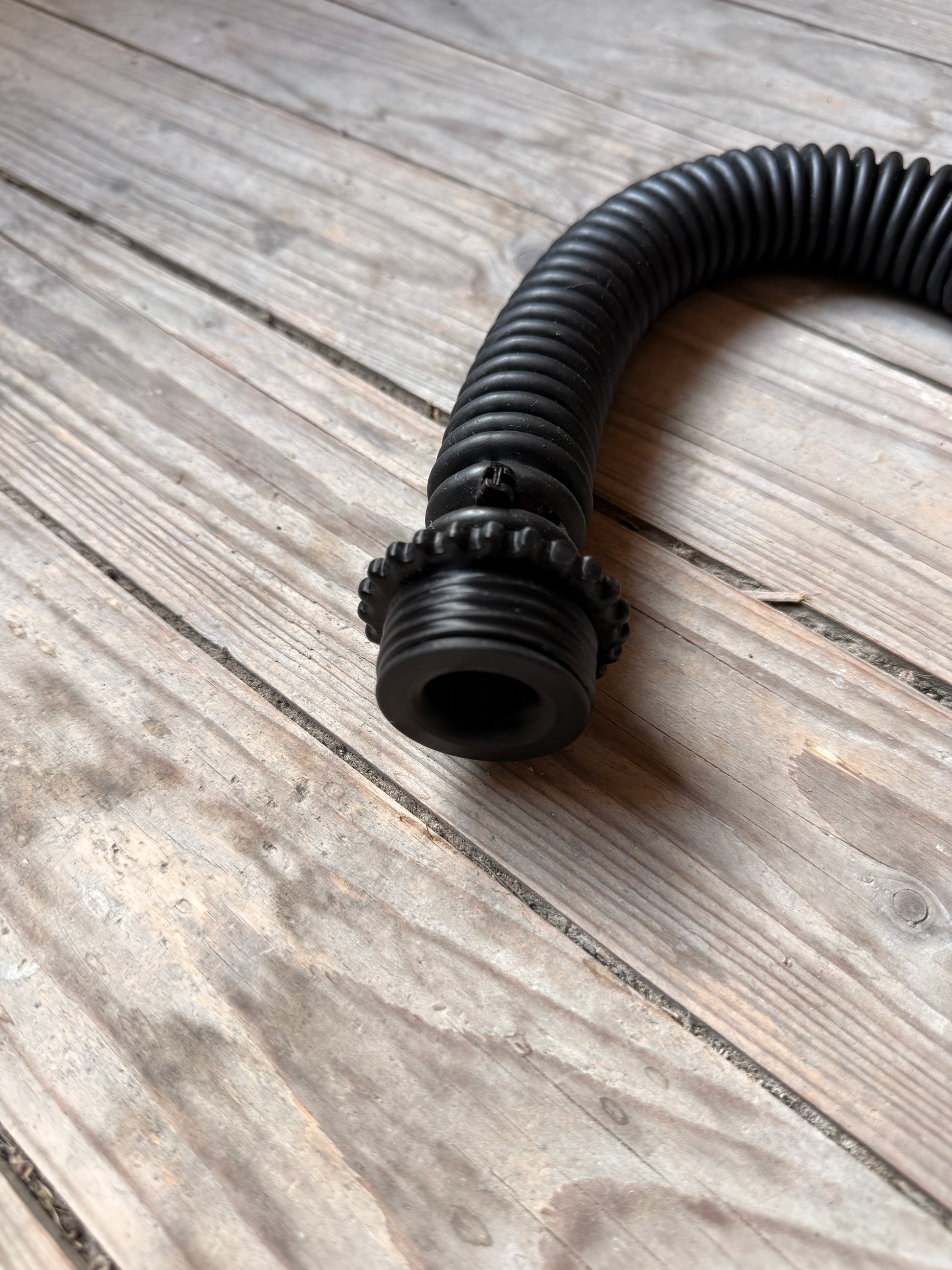 Detailaufnahme des schwarzen Vast Sniffer Schlauchs mit Schraubanschlüssen auf dem Holzboden.