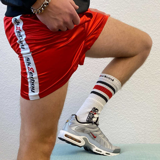 type sportif avec des sneakers Nike TN argentées et des chaussettes tube sk8erboy montre ses jambes et porte un boxer rouge brillant, avec une grosse chaîne de bras et une veste brillante